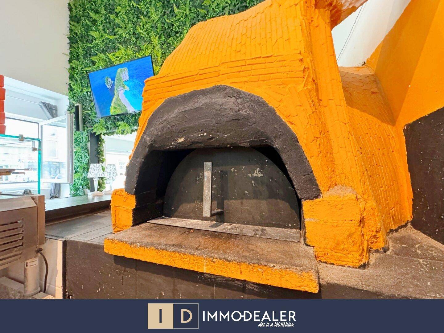 Großer, traditioneller Pizzaofen in leuchtendem Orange, umgeben von einer grünen Pflanzenwand.