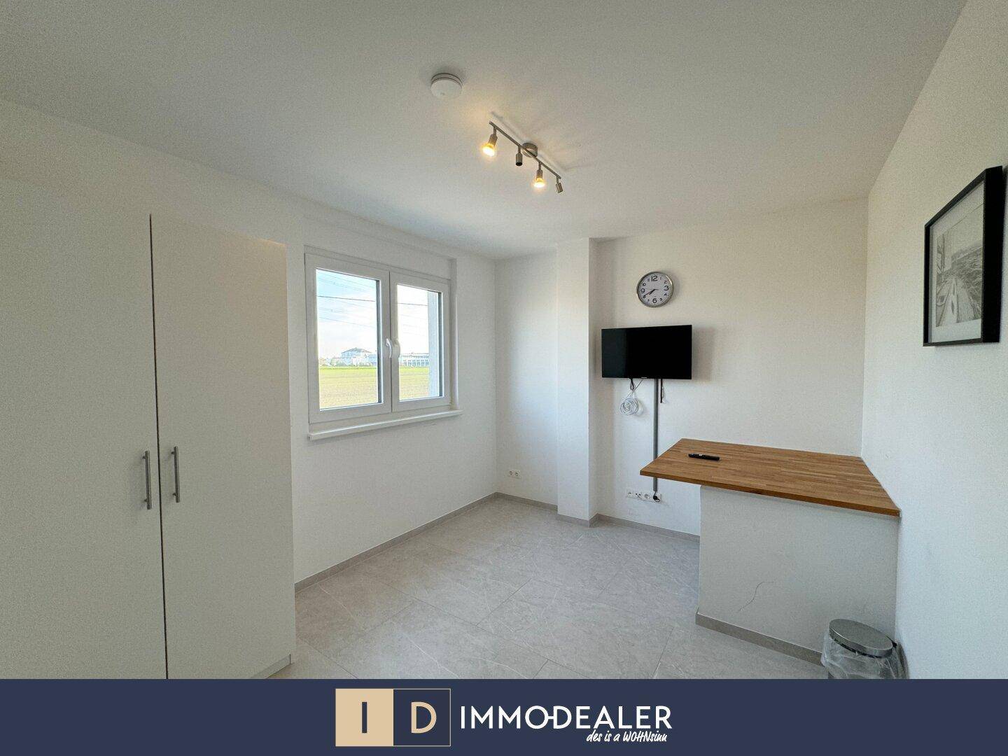 Helles Zimmer mit Fenster, Schrank und einem integrierten Schreibtisch, ideal als Schlaf- oder Arbeitszimmer.
