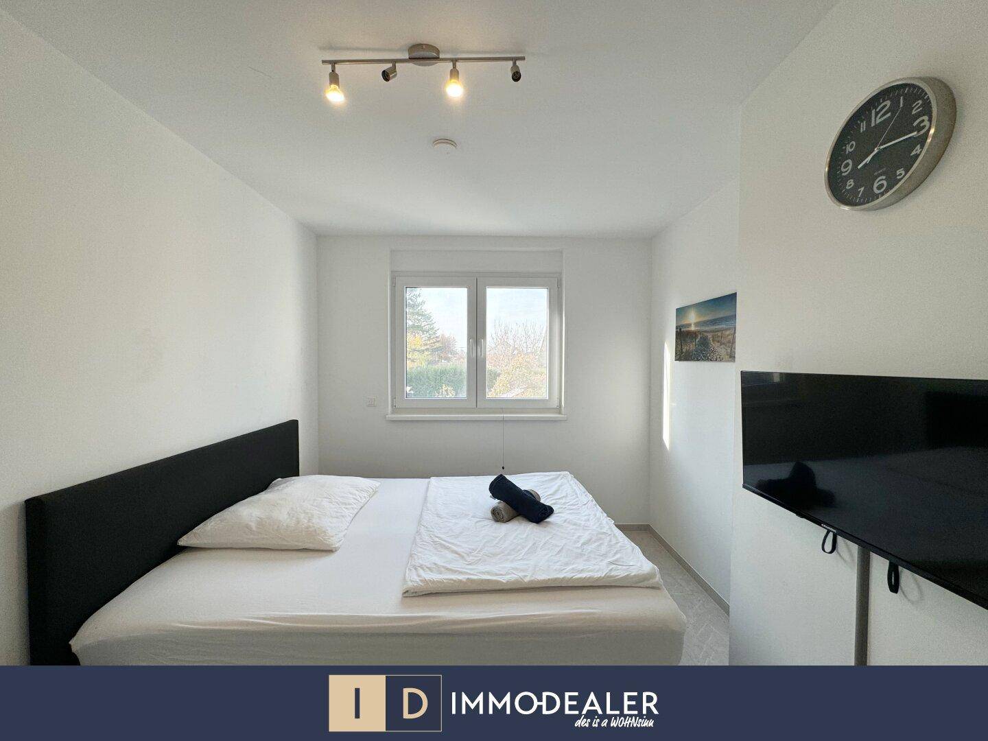 Gemütliches Schlafzimmer mit Doppelbett, Fenster und Wandfernseher, bietet viel Tageslicht.