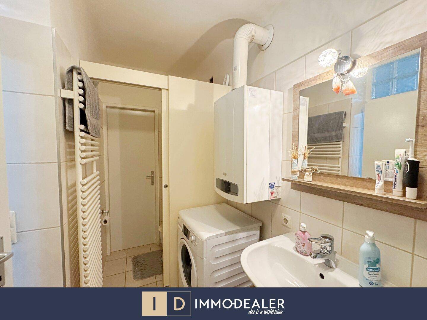 Helles Badezimmer mit Waschbecken, Spiegel, Waschmaschine und Heizkörper.