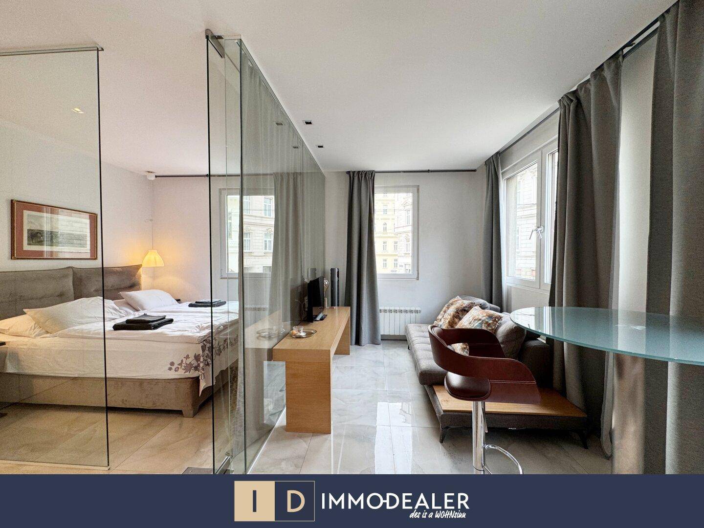 Studio-Apartment mit Schlafbereich, Sitzgelegenheit und Glasabtrennung.
