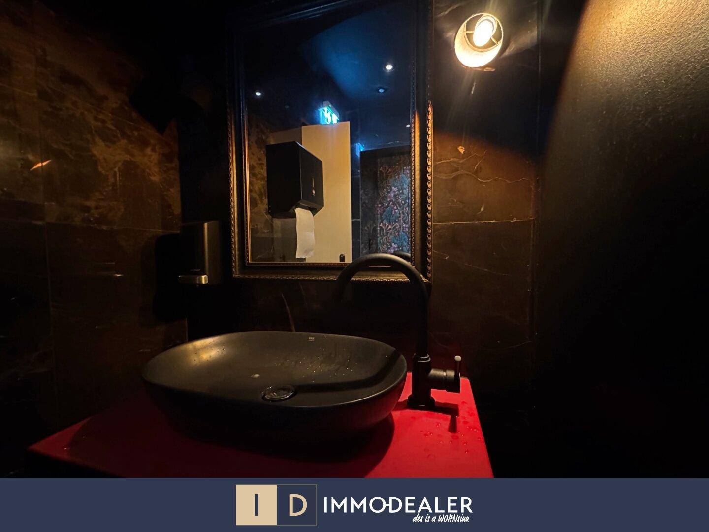 Modernes Waschbecken mit schwarzer Armatur und Spiegel in einem elegant gefliesten Toilettenraum mit dunklen Marmorfliesen.