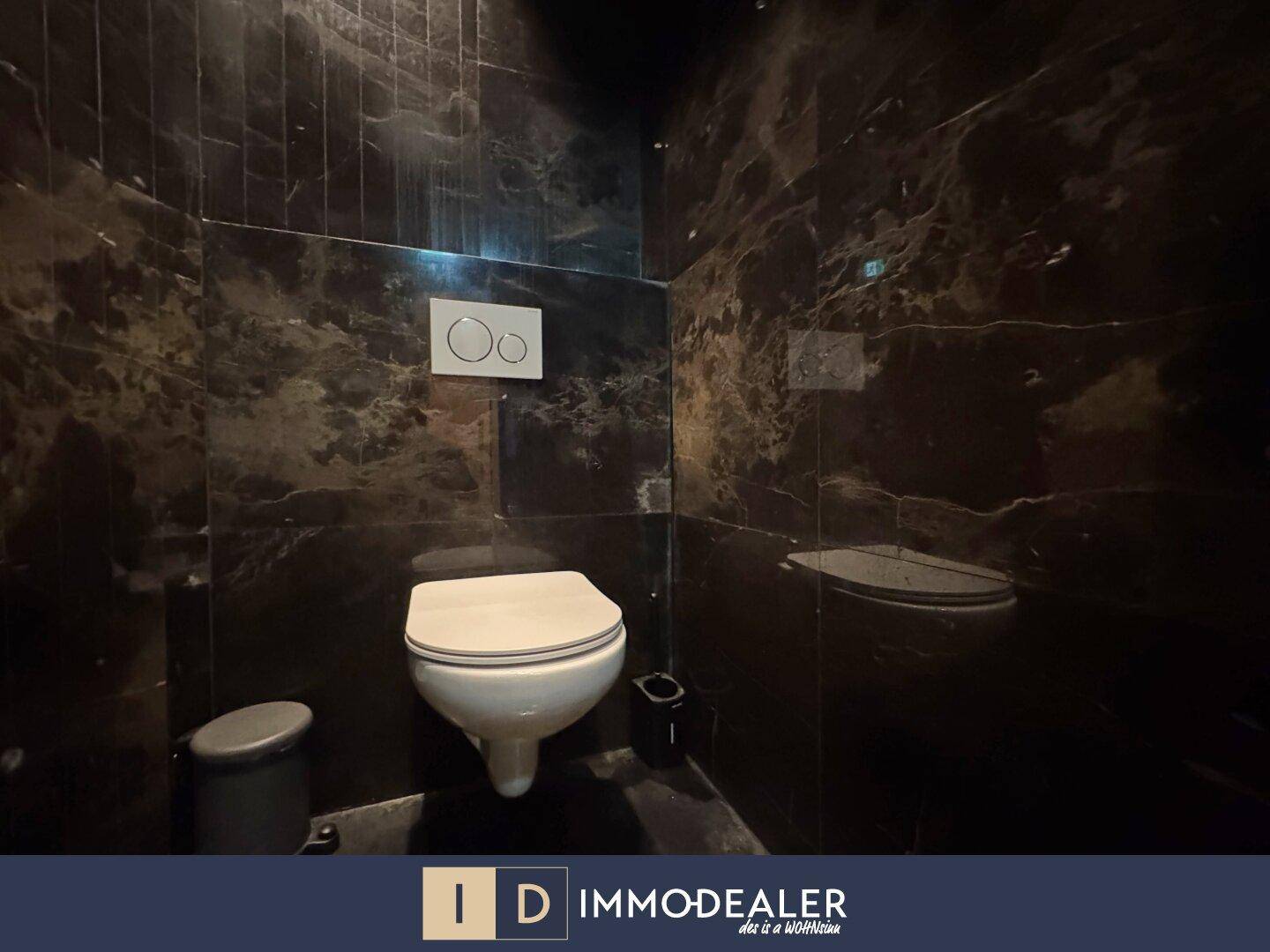 Wandhängende Toilette in einem luxuriösen Toilettenraum mit dunklen Marmorfliesen und minimalistischem Design.
