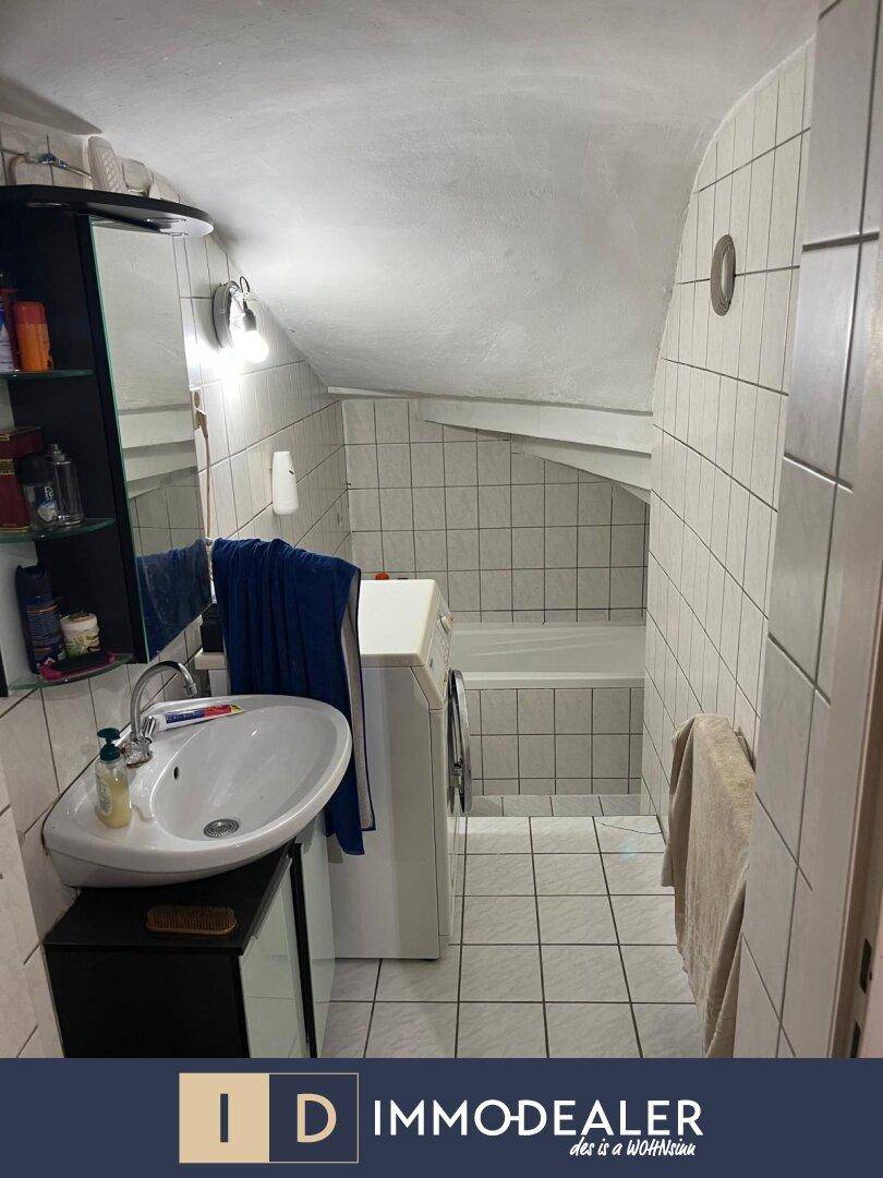 Badezimmer mit Waschbecken, Spiegelschrank und Waschmaschine unter einer Dachschräge.