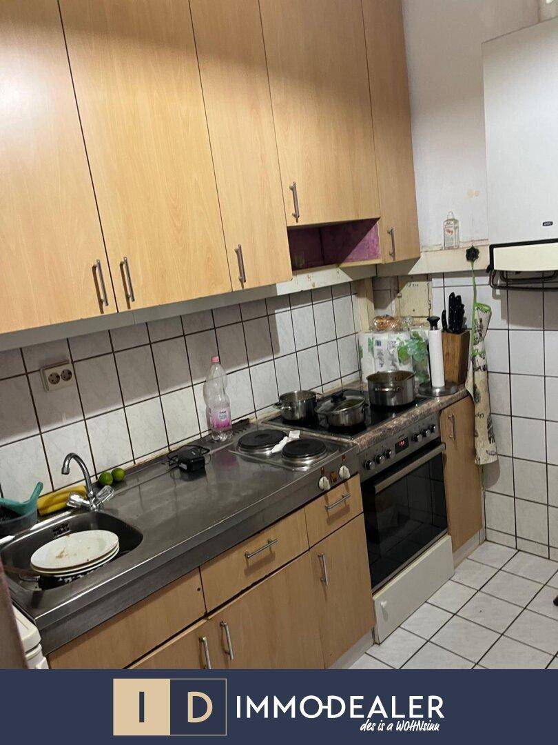 Küche mit Holzschränken, Edelstahlspüle und Herd, gefliestem Spritzschutz und Boden.