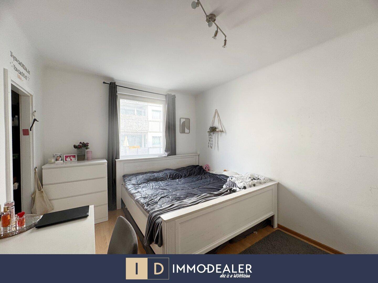 Schlafzimmer mit Doppelbett, Kommode und Fenster, das Tageslicht hereinlässt.