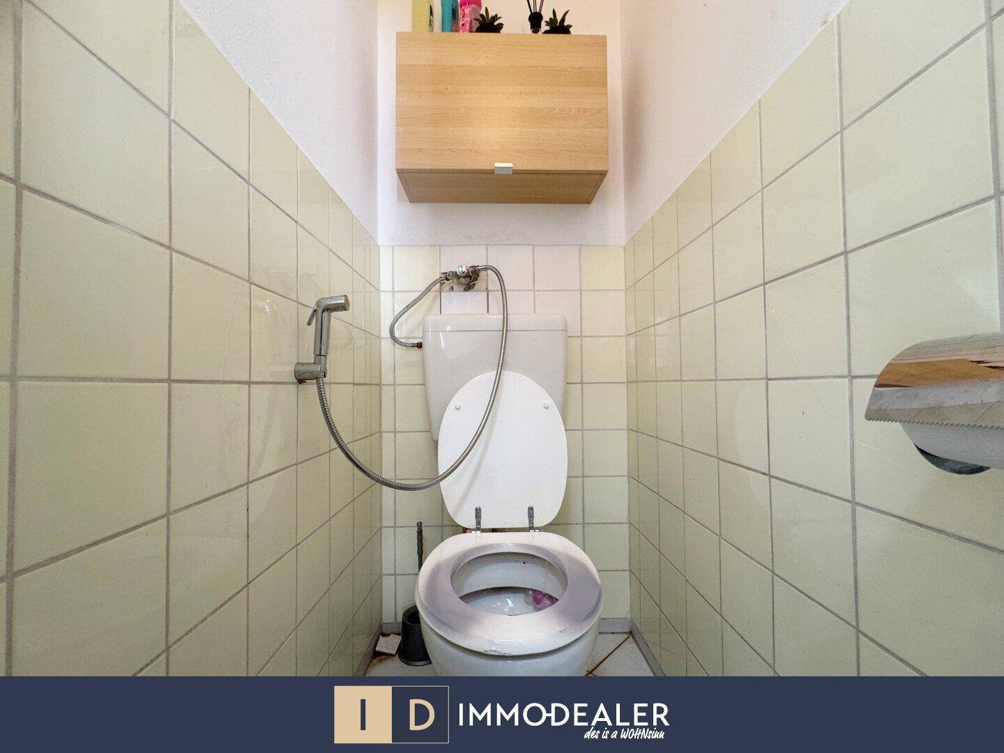 Separate Toilette mit hellen Fliesen und einem kleinen Hängeschrank.