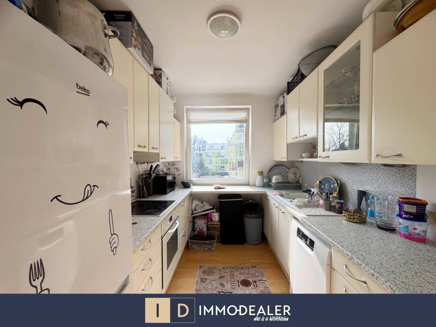 Funktionale Küche mit weißen Schränken, Arbeitsplatte und Fenster mit Blick nach draußen.