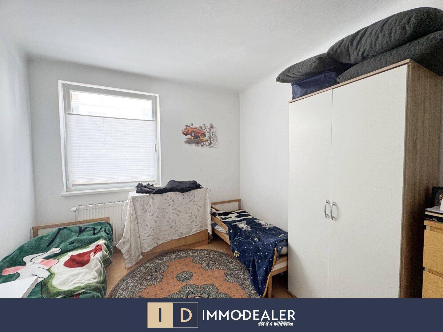 Kinderzimmer mit zwei Betten, Kleiderschrank und Fenster mit Jalousie.