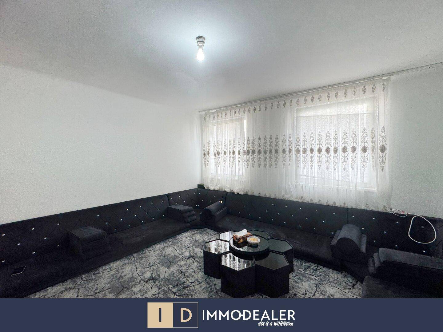 Geräumiges Wohnzimmer mit großem Ecksofa, Teppich und zwei Fenstern.