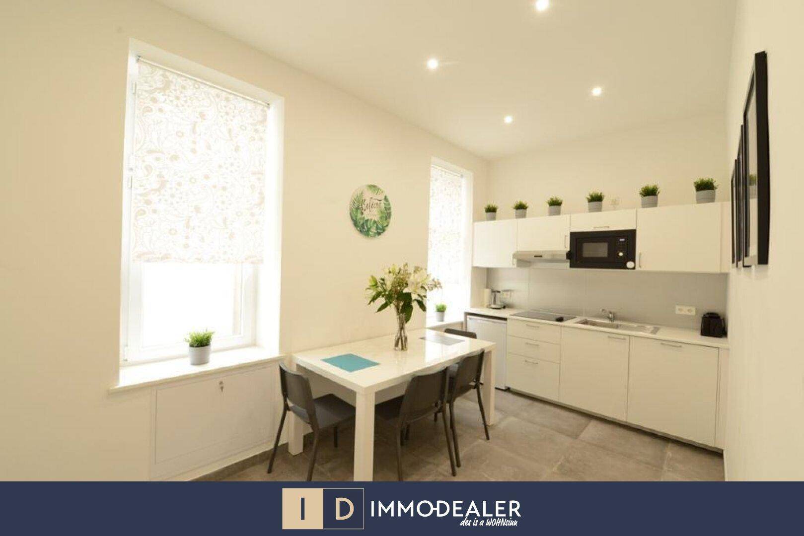 Moderne weiße Küche mit Essbereich, Einbaugeräten und großen Fenstern.