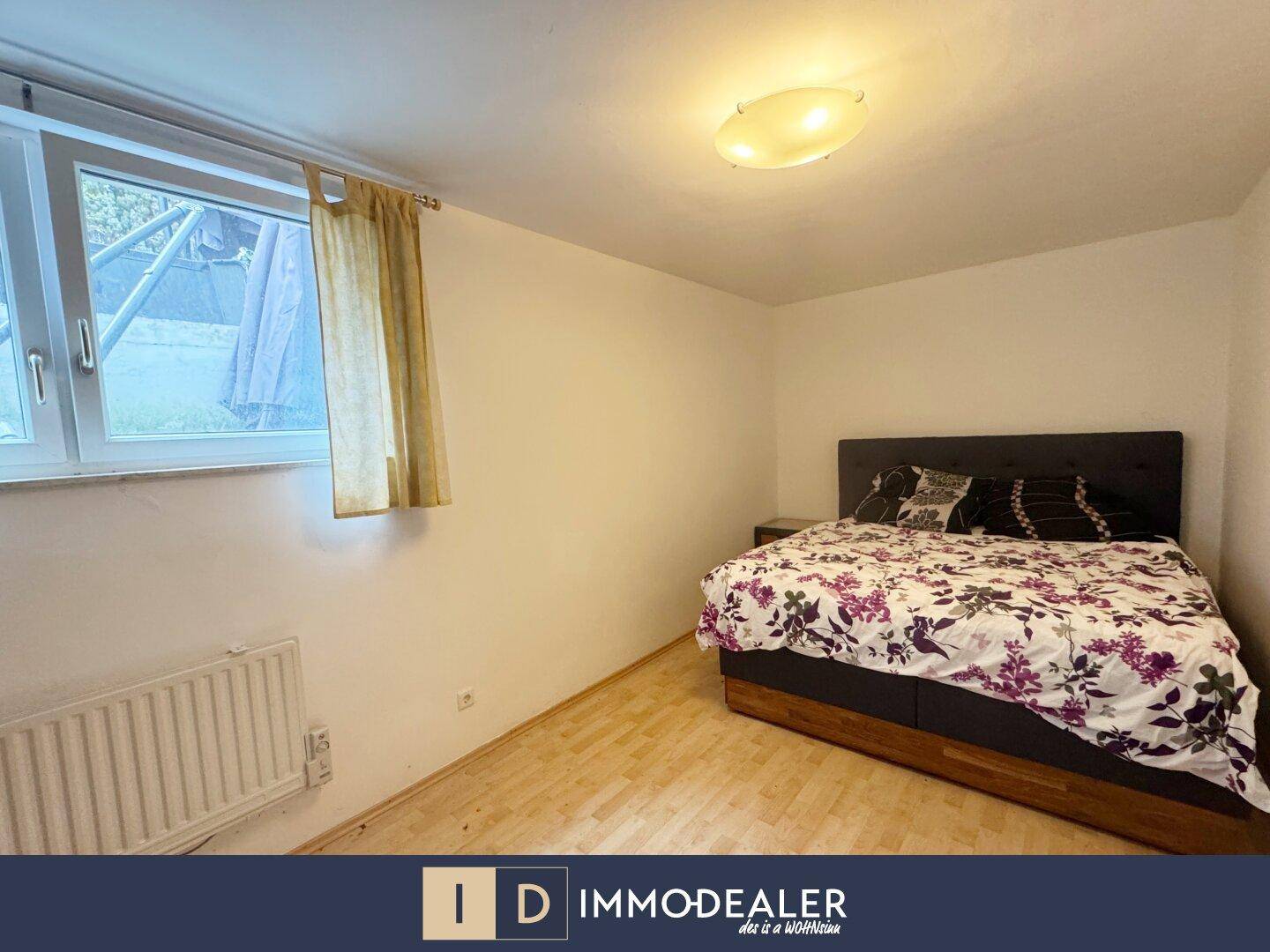 Schlafzimmer mit Doppelbett und Holzfußboden, ausgestattet mit einem Fenster und Heizkörper.