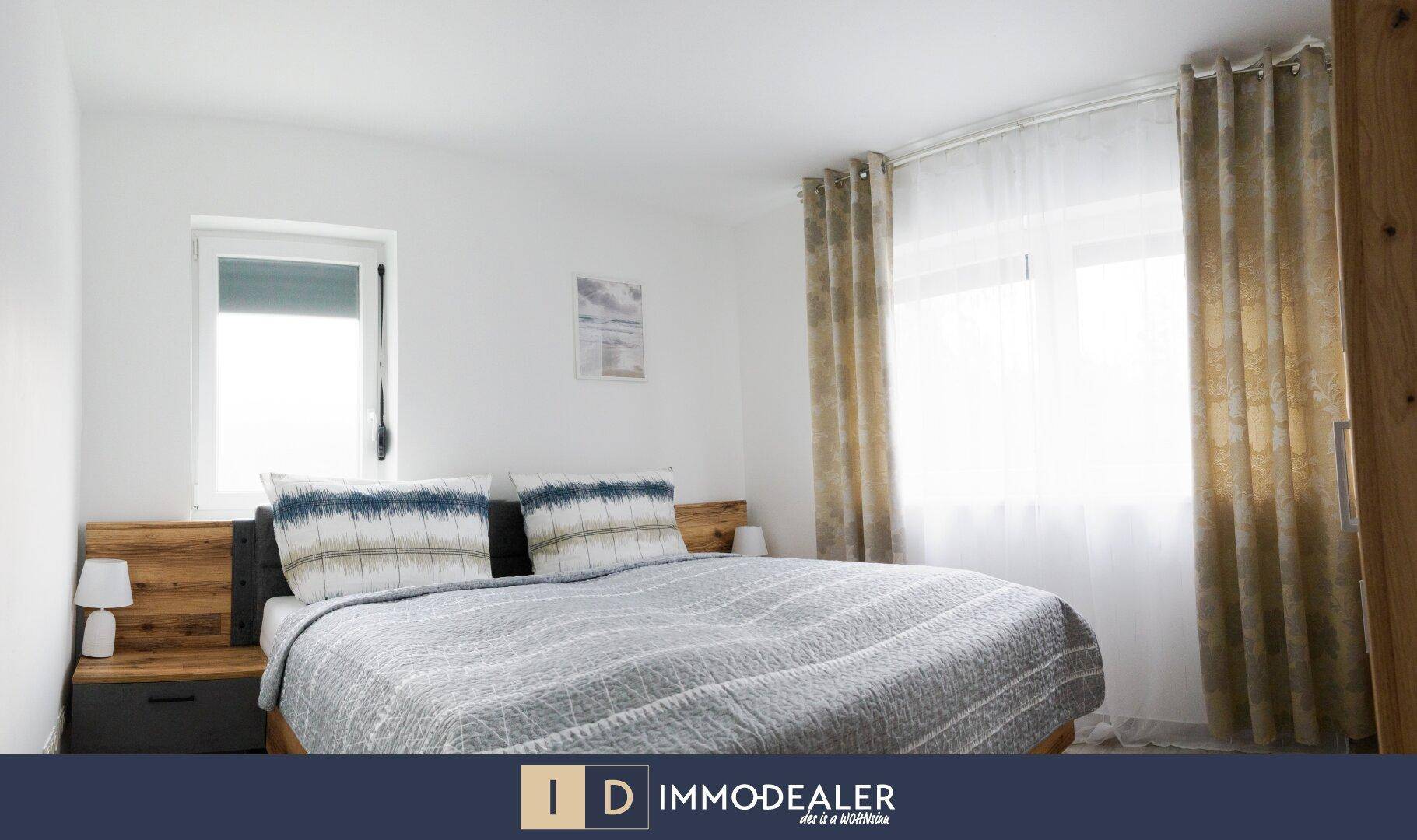 Gemütliches Schlafzimmer mit Doppelbett, Holzelementen und großen Fenstern für viel natürliches Licht.