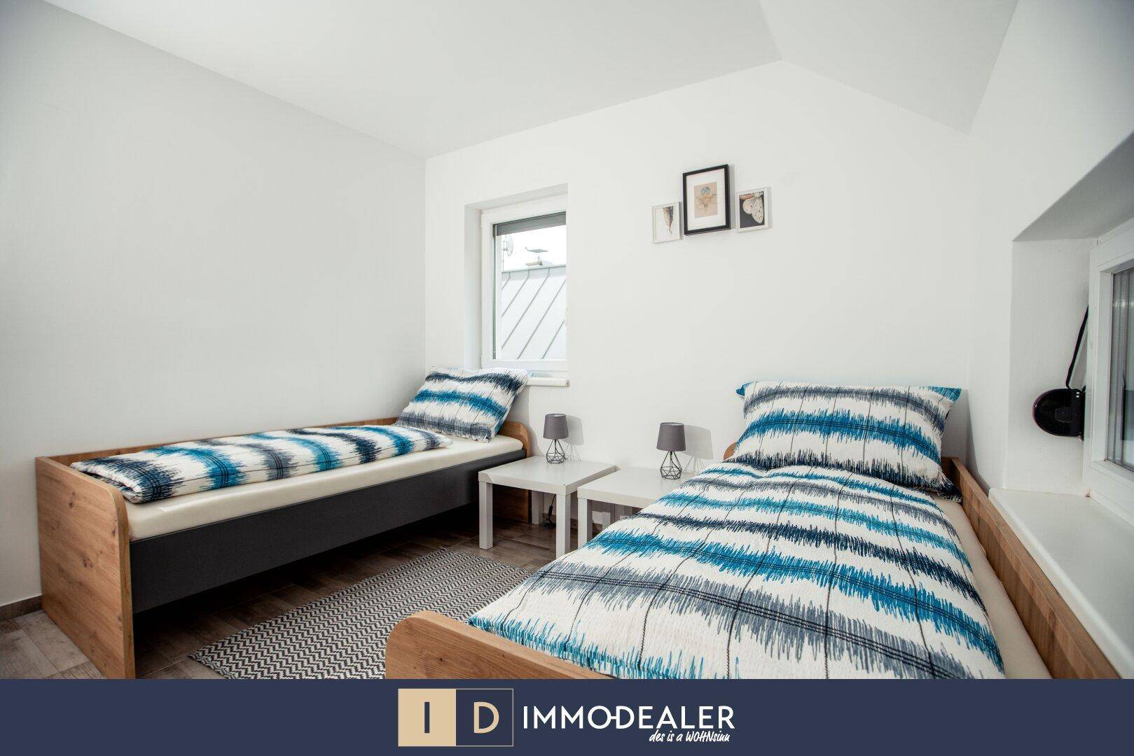 Helles Schlafzimmer mit zwei Einzelbetten, Nachttischen und Blick ins Grüne durch das Fenster.