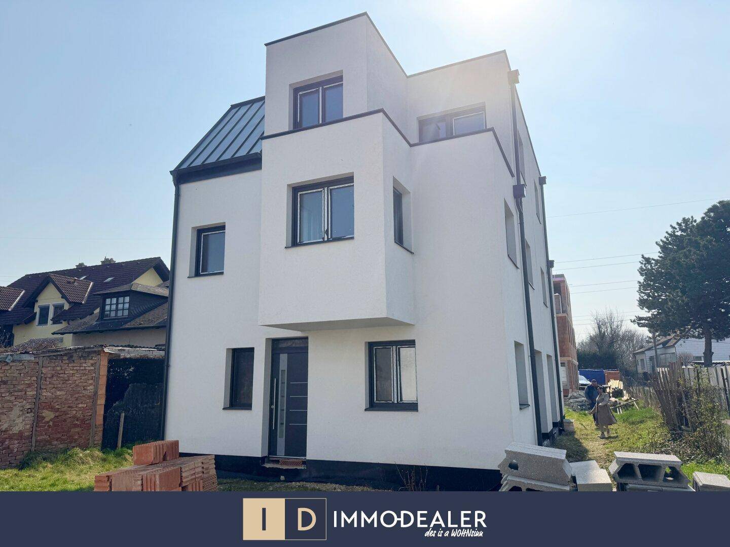 Neubau mit moderner Architektur, weißer Fassade und dunklem Dach, umgeben von Baustellenmaterial.