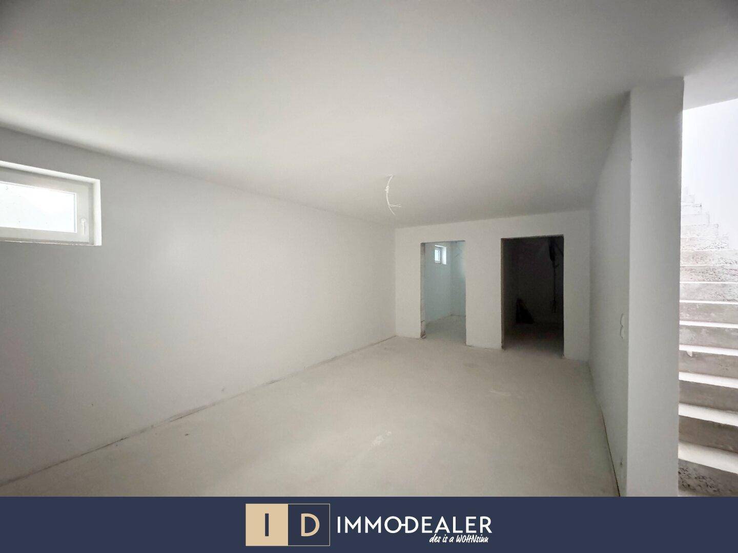 Geräumiger Kellerraum im Rohbau mit einem kleinen Fenster und einer Treppe, die nach oben führt.