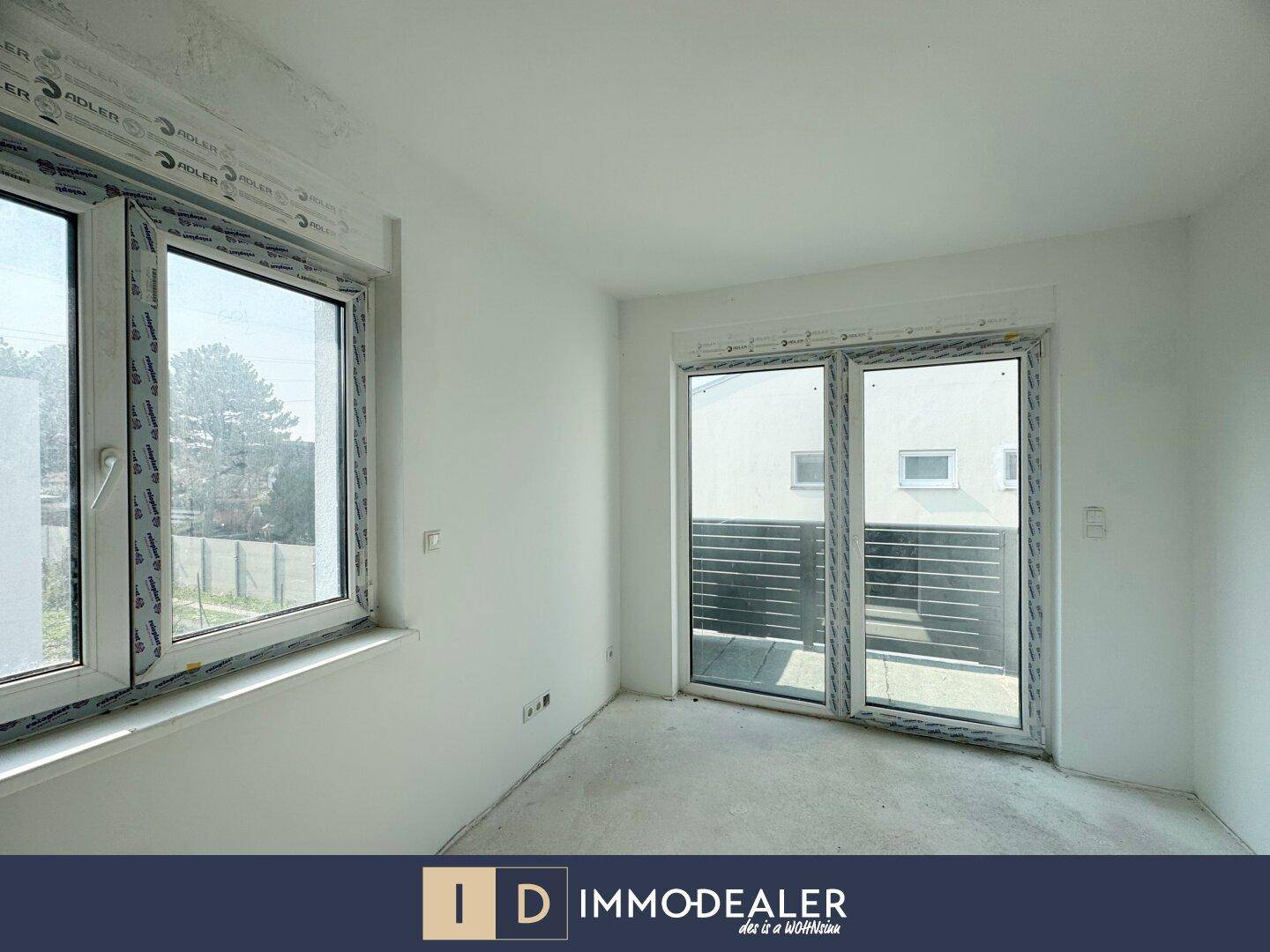 Heller Raum im Rohbau mit großem Fenster und Zugang zu einem Balkon, ideal für Wohnzwecke.