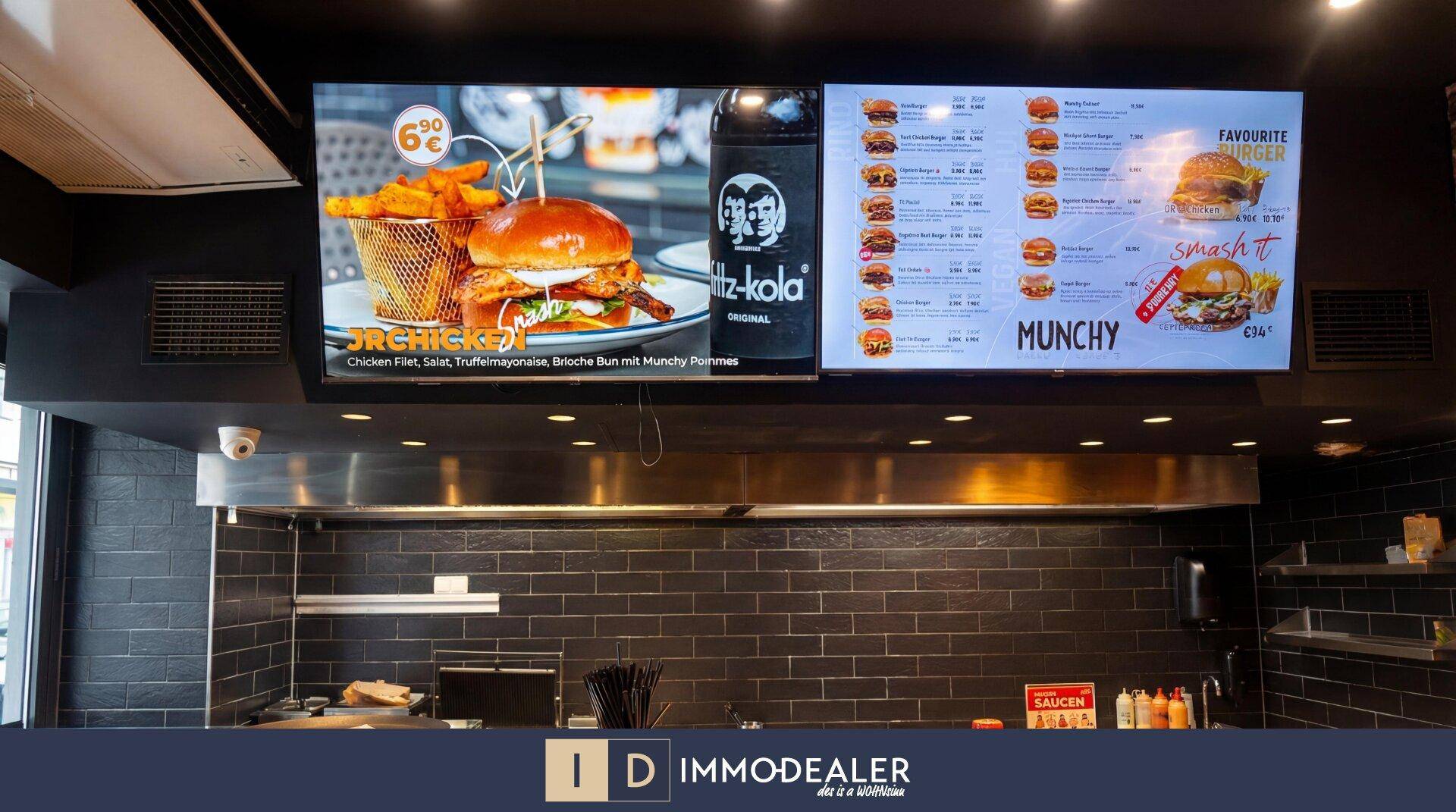 Digitale Menütafeln über der professionellen Küche, die Speisen und Preise des Restaurants anzeigen.