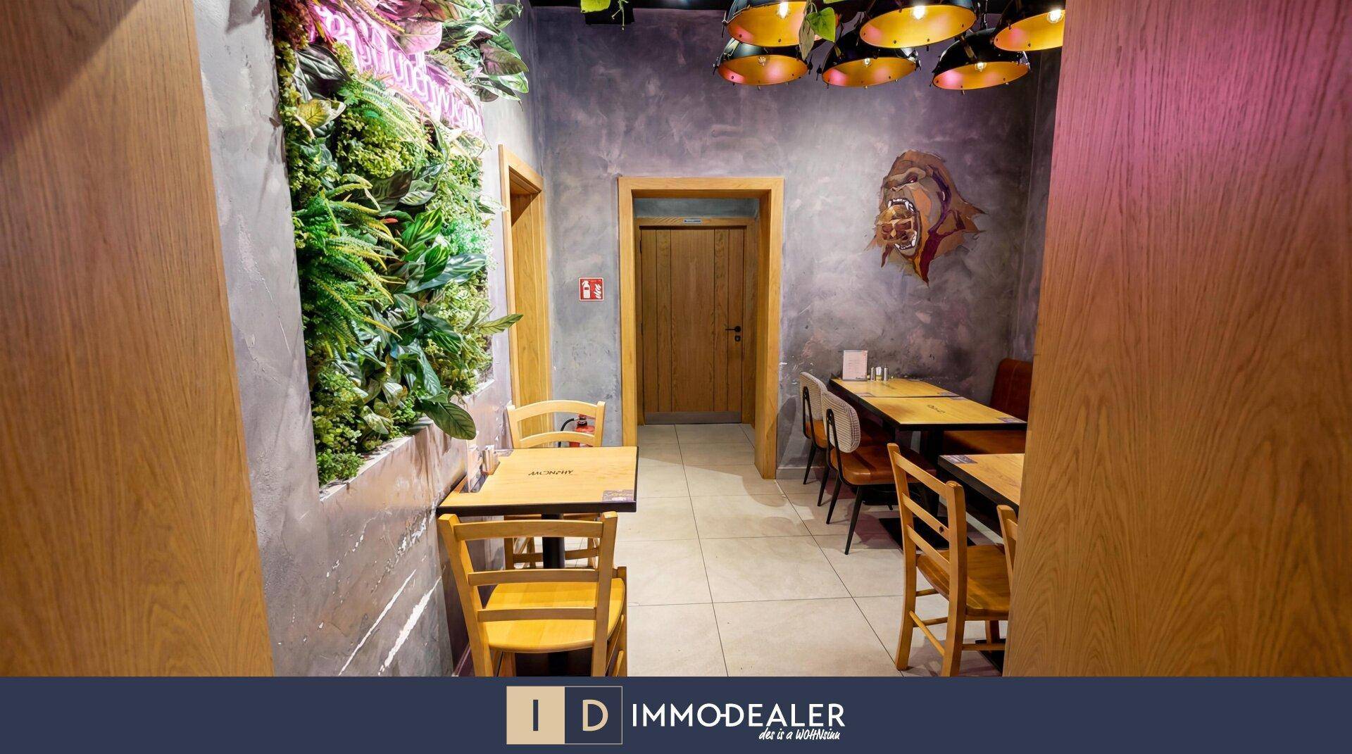 Restaurant-Sitzbereich mit grüner Pflanzenwand, Holztüren und industriellen Hängelampen, die eine einladende Atmosphäre schaffen.