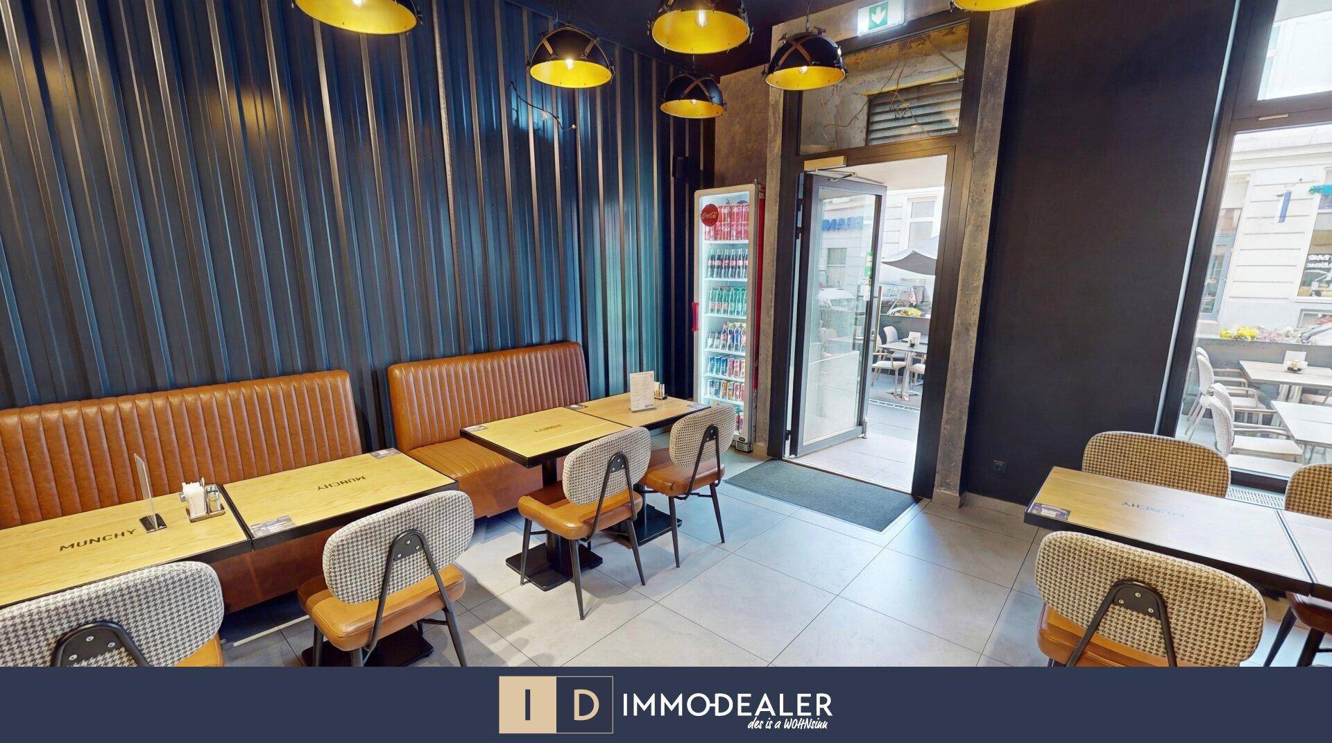 Innenansicht des Restaurants mit Sitzbänken, Tischen und Blick auf den Eingangsbereich und die Straße.