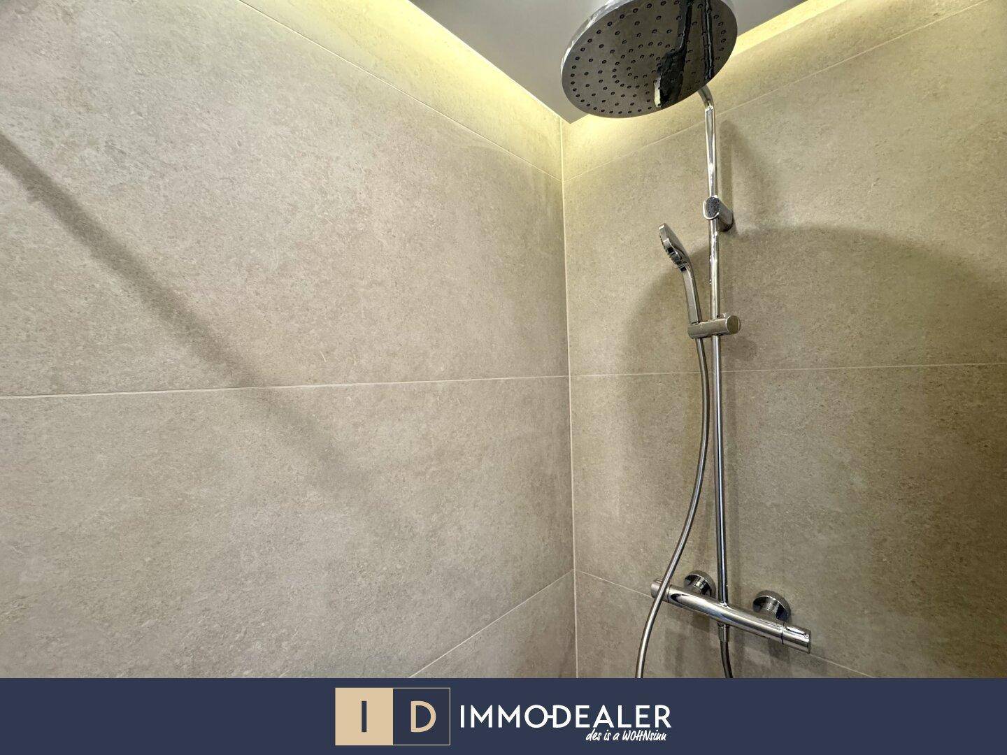 Nahaufnahme einer modernen Regendusche mit Handbrause und beigefarbenen Wandfliesen im Badezimmer.
