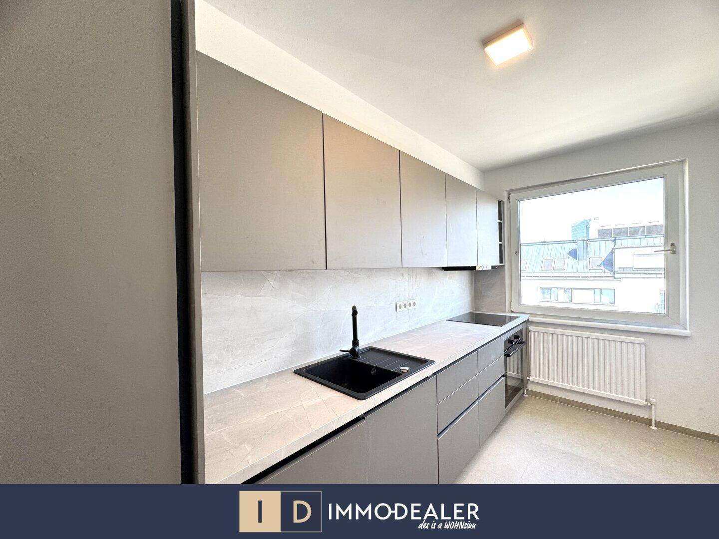 Moderne Küche mit grauen Schränken, integriertem Backofen und einem Fenster für natürliche Belichtung.