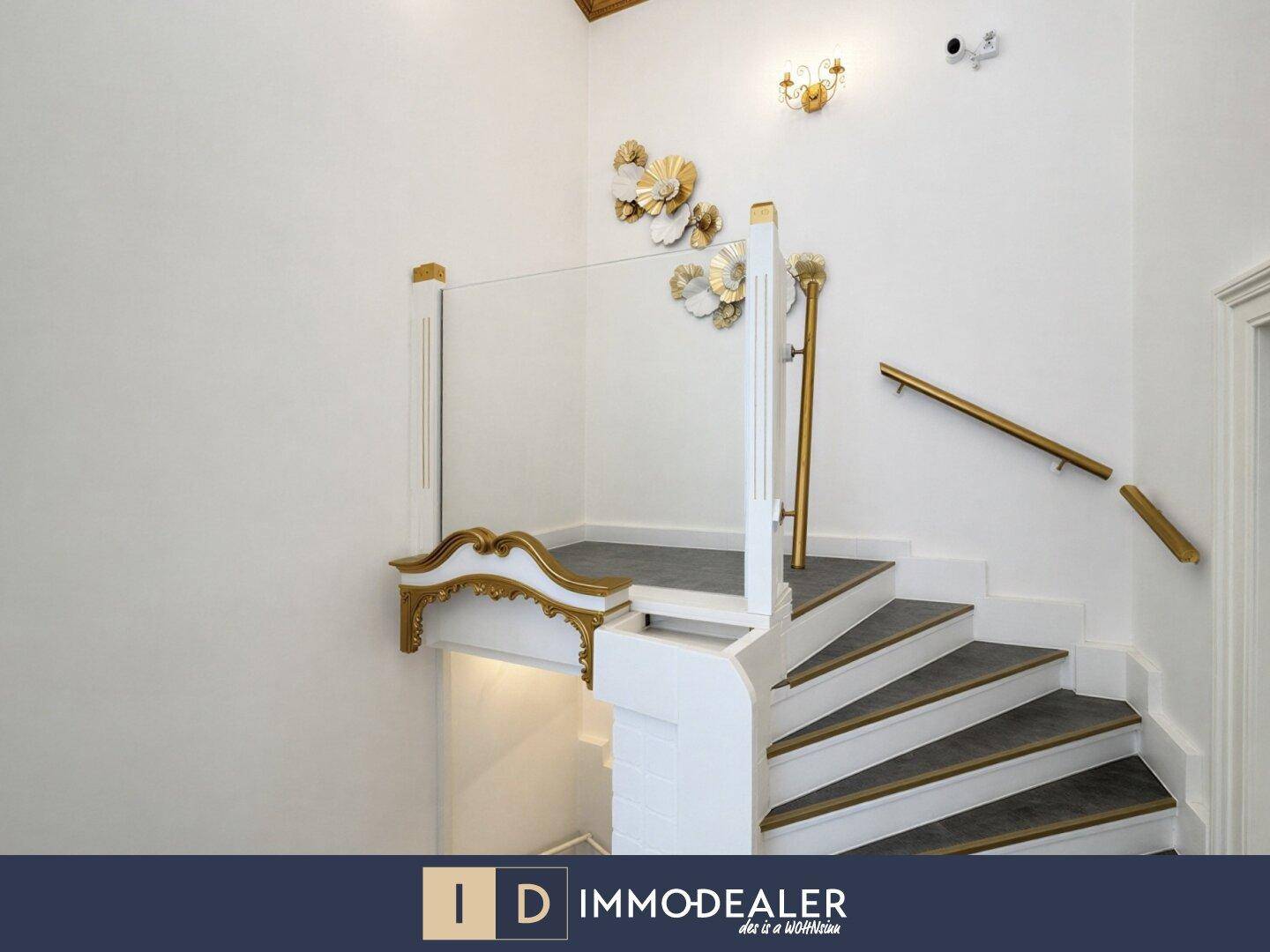 Elegante Treppe mit Glasgeländer, goldenen Handläufen und dekorativen Wandelementen, die zum Obergeschoss führt.
