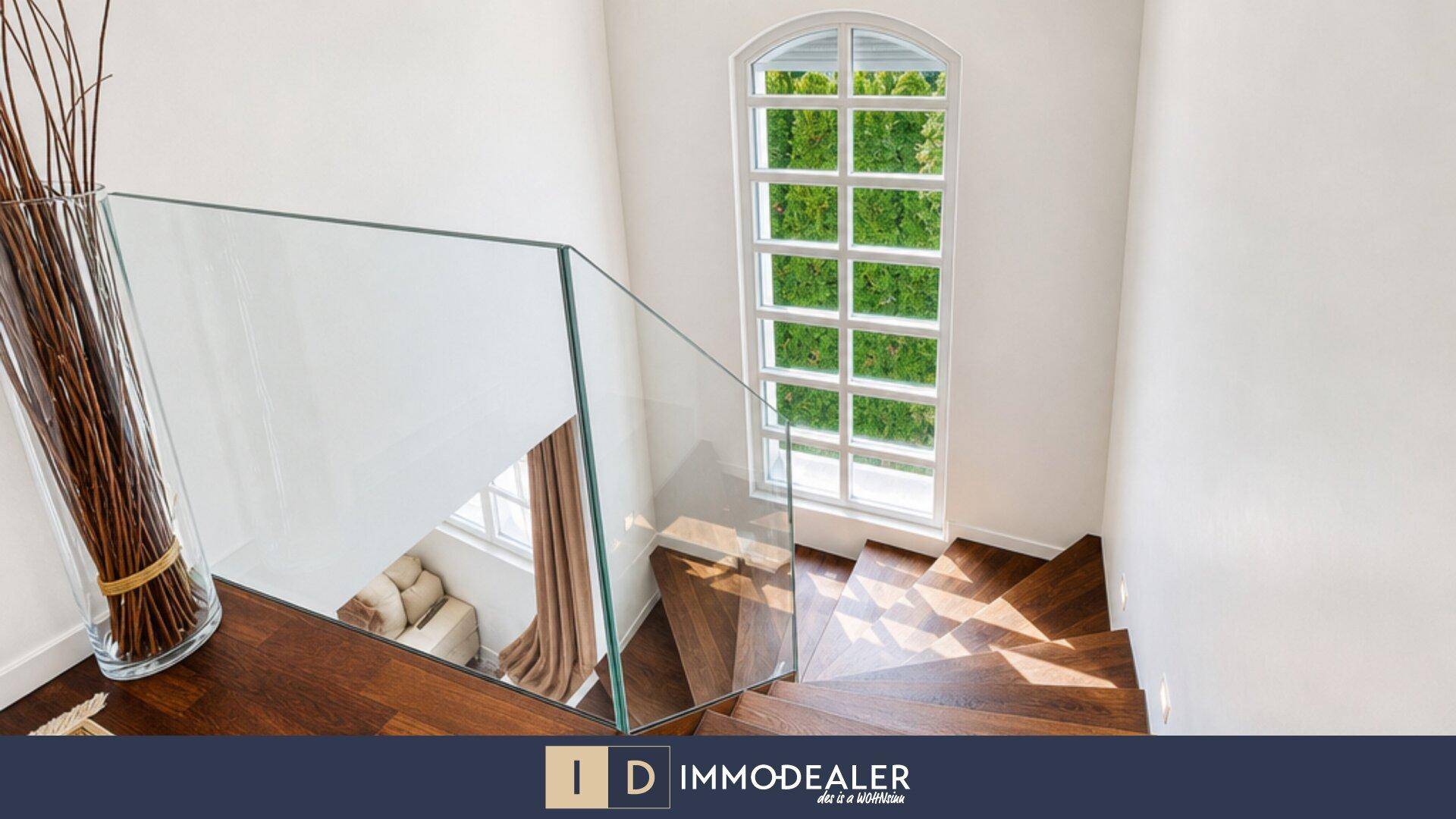 Elegante Holztreppe mit Glasgeländer und großen Fenstern, die den Flur erhellen.