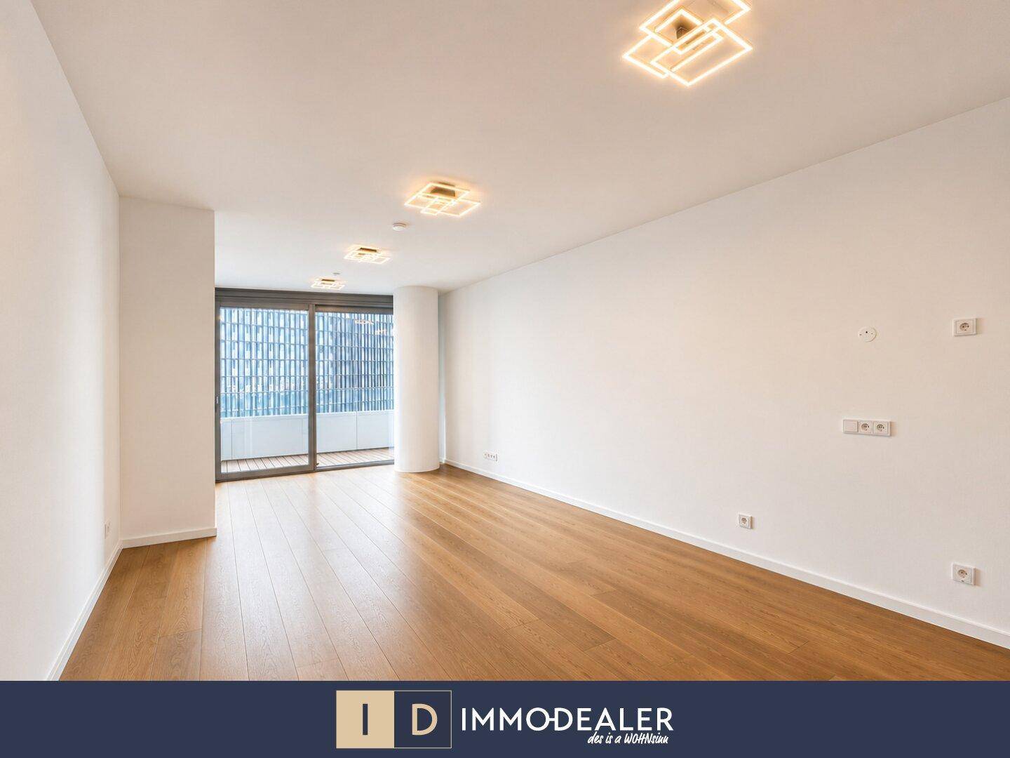 Heller, leerer Wohnraum mit Holzboden, weißen Wänden und Zugang zu einem Balkon.