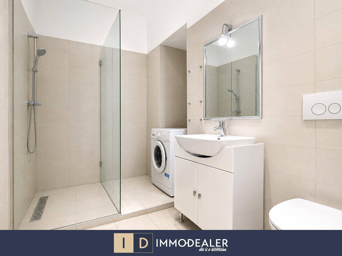 Modernes Badezimmer mit ebenerdiger Dusche, Waschbecken und Waschmaschine, hell gefliest.