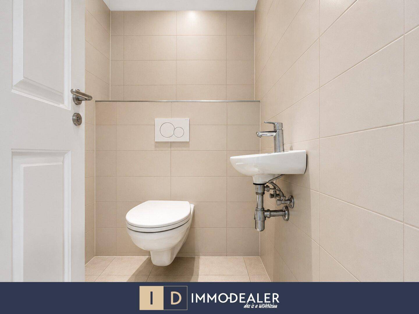 Separates Gäste-WC mit Wand-WC und kleinem Waschbecken, in hellen Fliesen gehalten.
