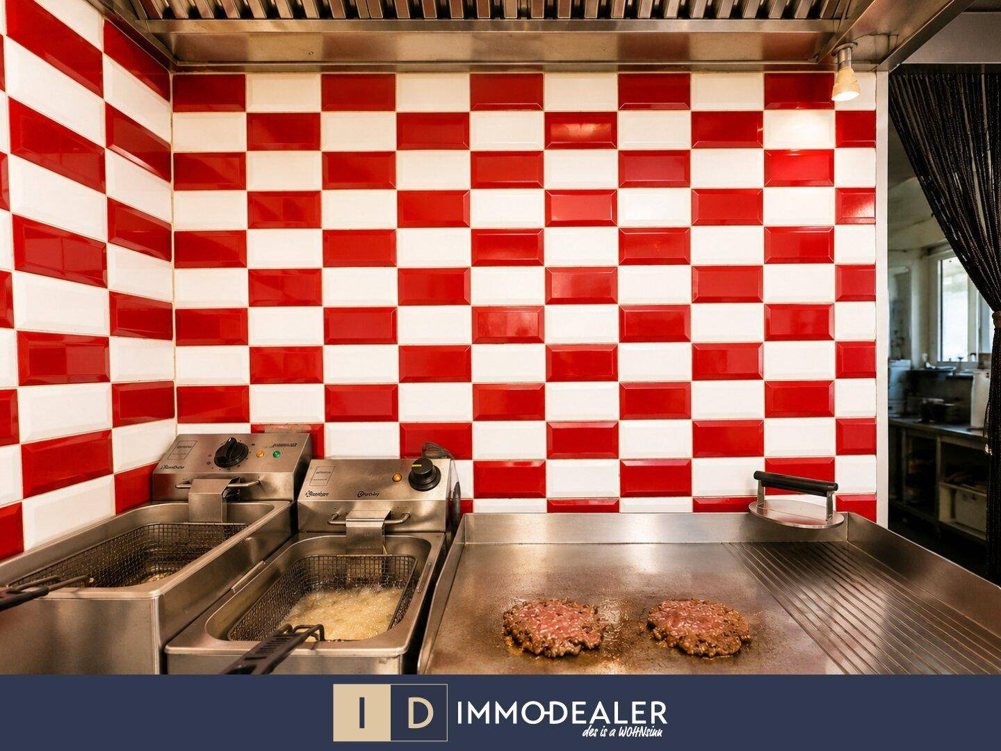 Detailansicht der professionellen Küche mit Fritteusen, Grillplatte und rot-weiß gefliesten Wänden.
