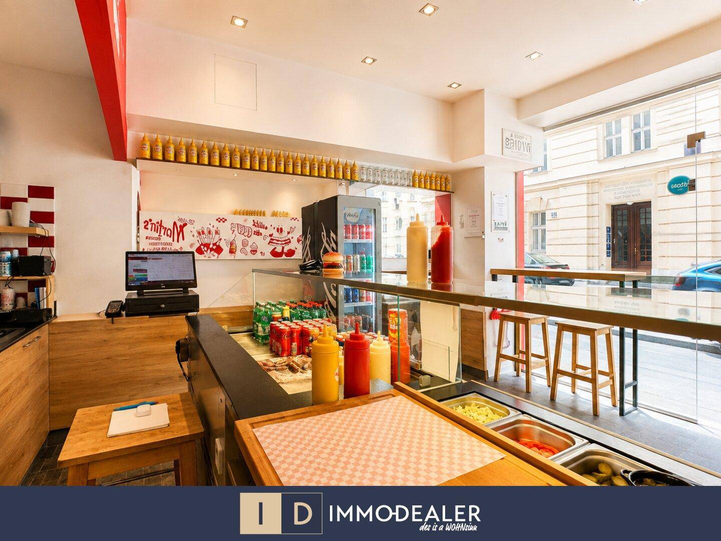 Innenansicht des Schnellrestaurants mit Blick zur Straße, Theke und Sitzhockern.