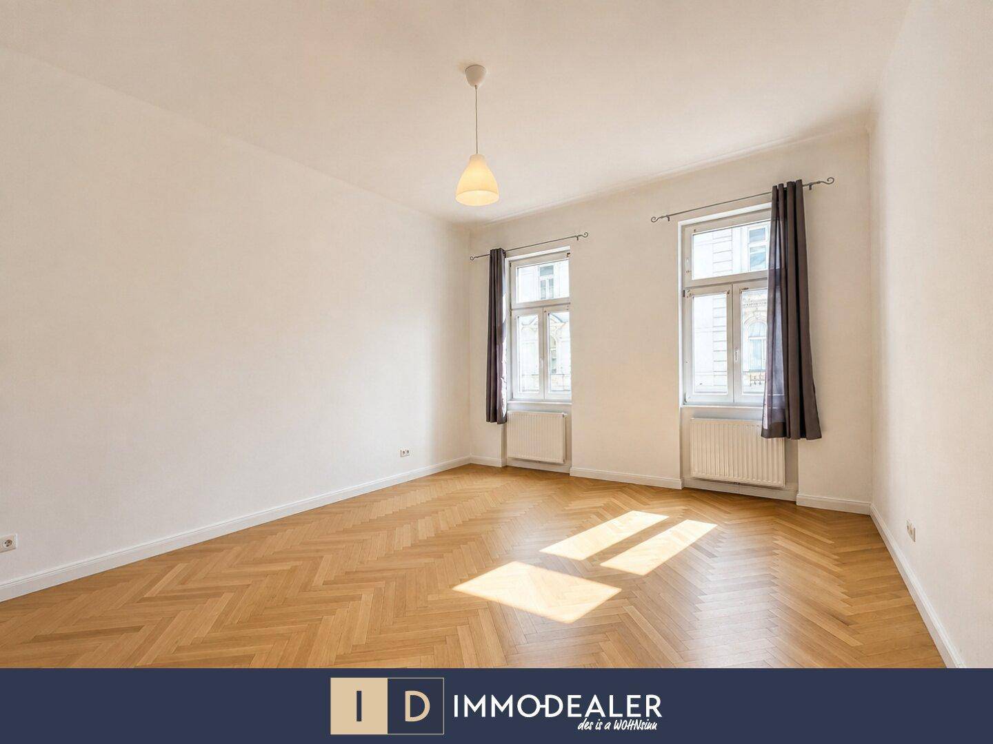 Geräumiges Zimmer mit hellem Fischgrätparkett und zwei Fenstern, die den Raum erhellen.