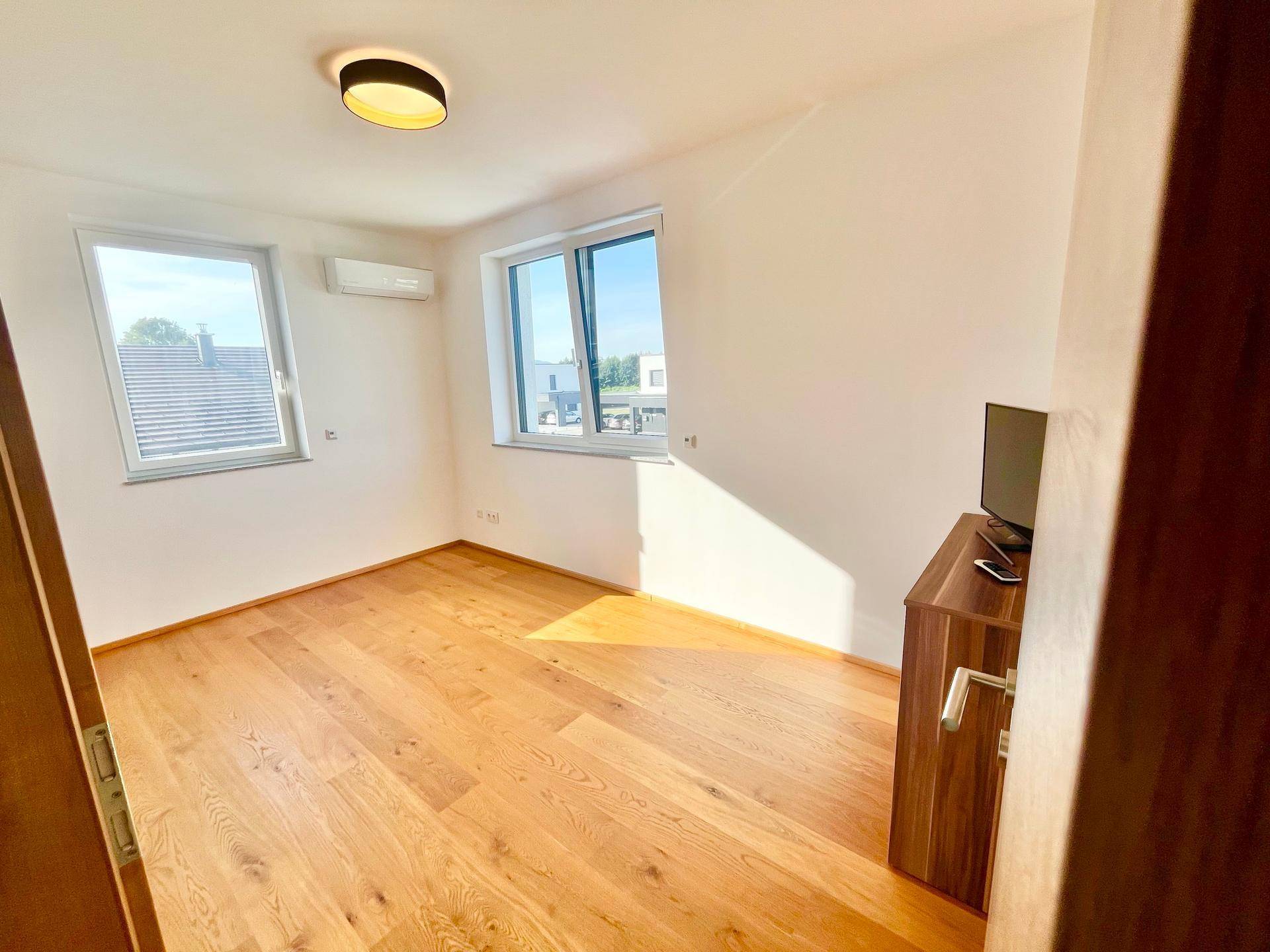 Helles Schlafzimmer mit Holzboden, weißen Wänden und Klimaanlage.