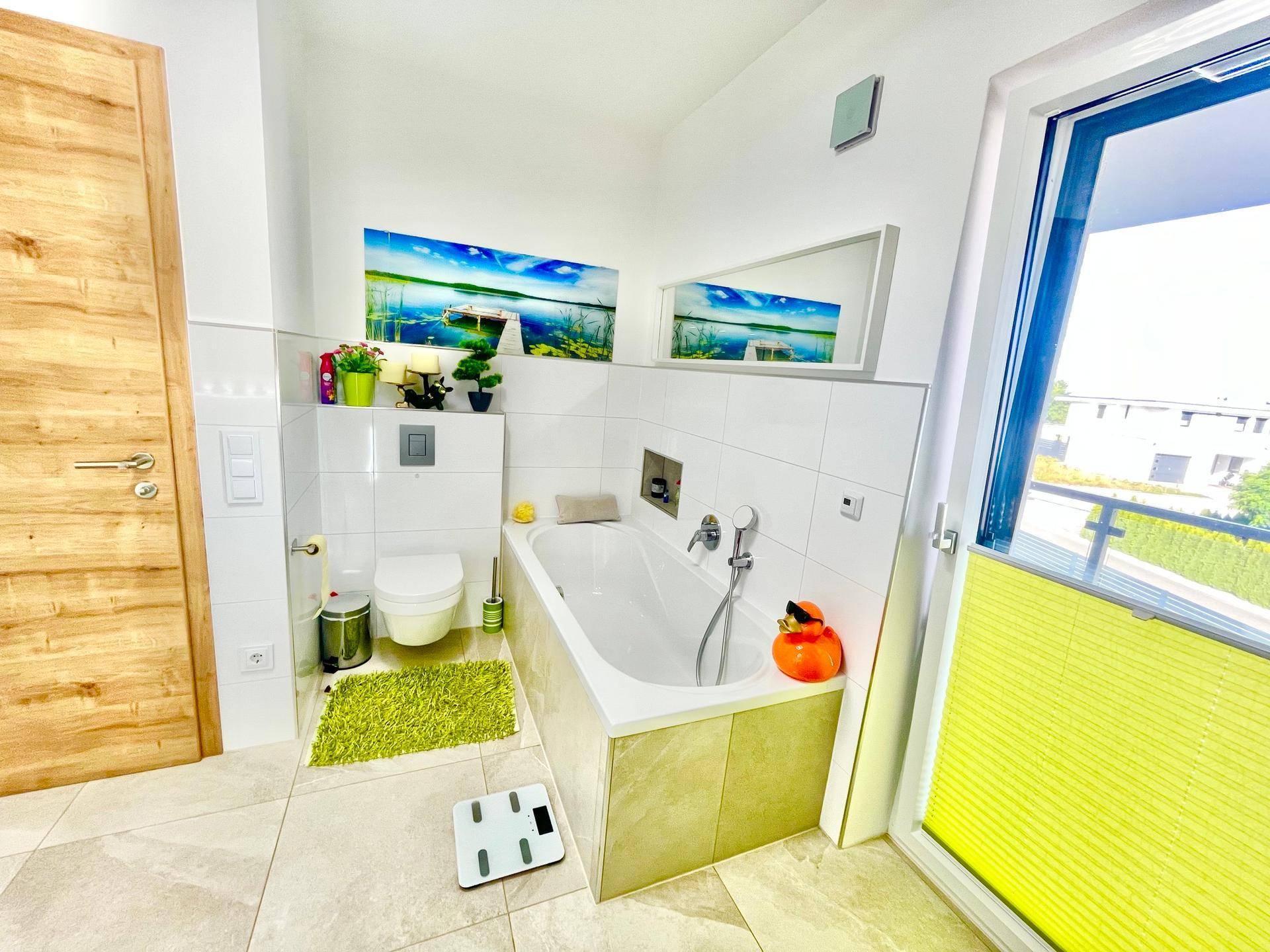 Helles Badezimmer mit Badewanne, wandhängendem WC und Fenster, das viel Tageslicht hereinlässt.