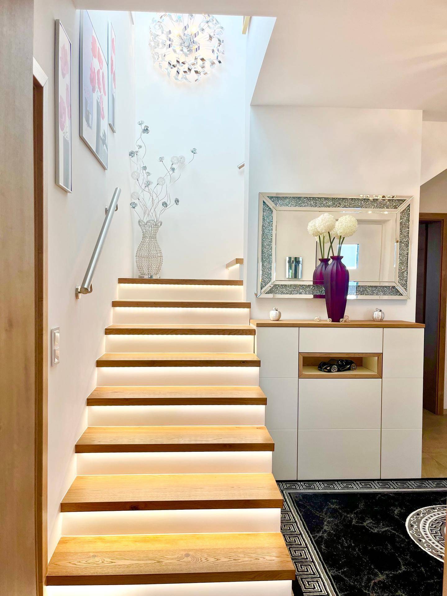 Moderner Eingangsbereich mit beleuchteter Holztreppe und stilvollem Spiegel.