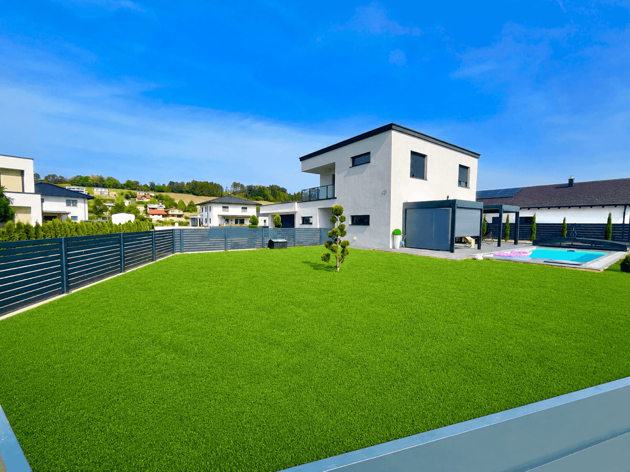 Großer, gepflegter Garten mit Rasenfläche, Pool und überdachtem Terrassenbereich hinter dem modernen Haus.