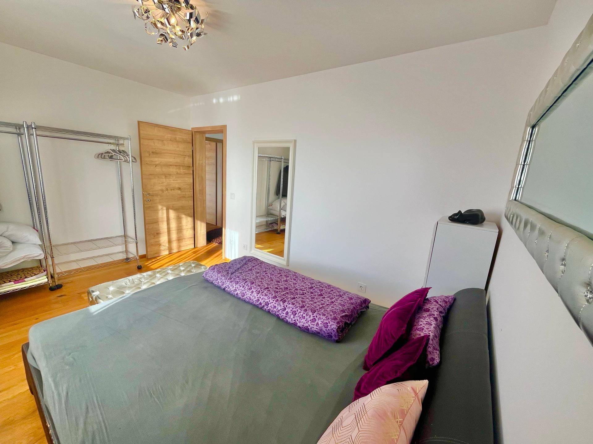 Schlafzimmer mit Holzboden, großem Bett und Zugang zu einem weiteren Raum.