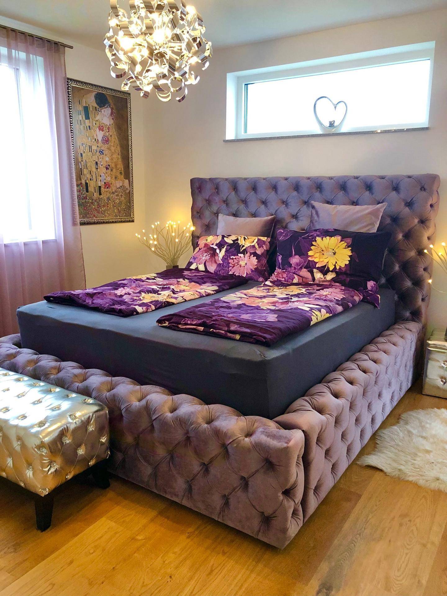 Elegantes Schlafzimmer mit gepolstertem Bett, Holzboden und dekorativer Beleuchtung.