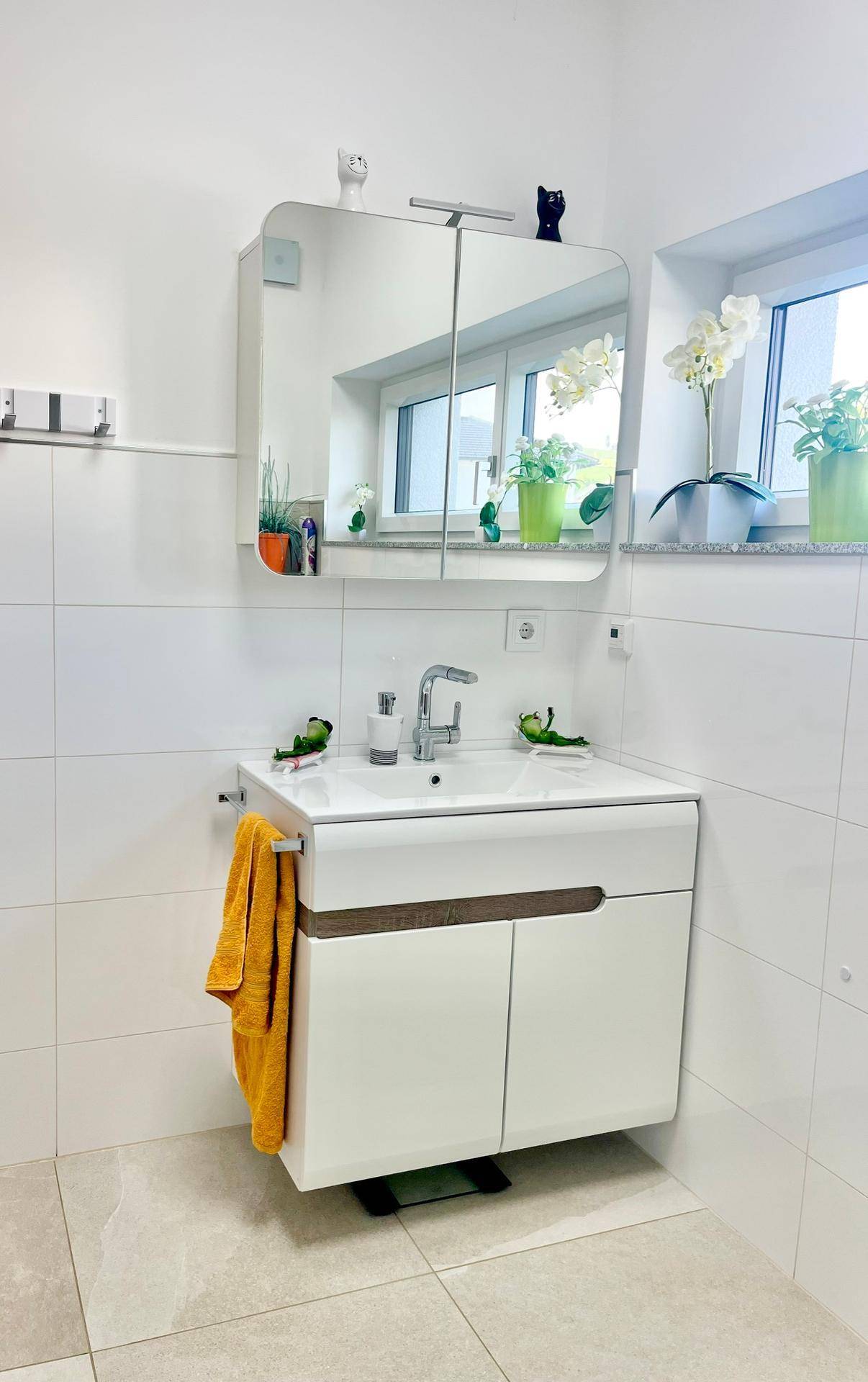 Modernes Badezimmer mit Waschtisch, Spiegelschrank und Fenster für Tageslicht.