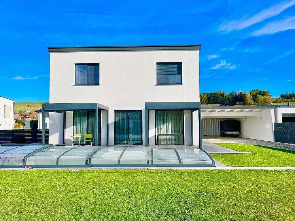 Rückseite des Hauses mit großen Glasfronten, überdachter Terrasse und einem Pool mit Schiebeabdeckung.