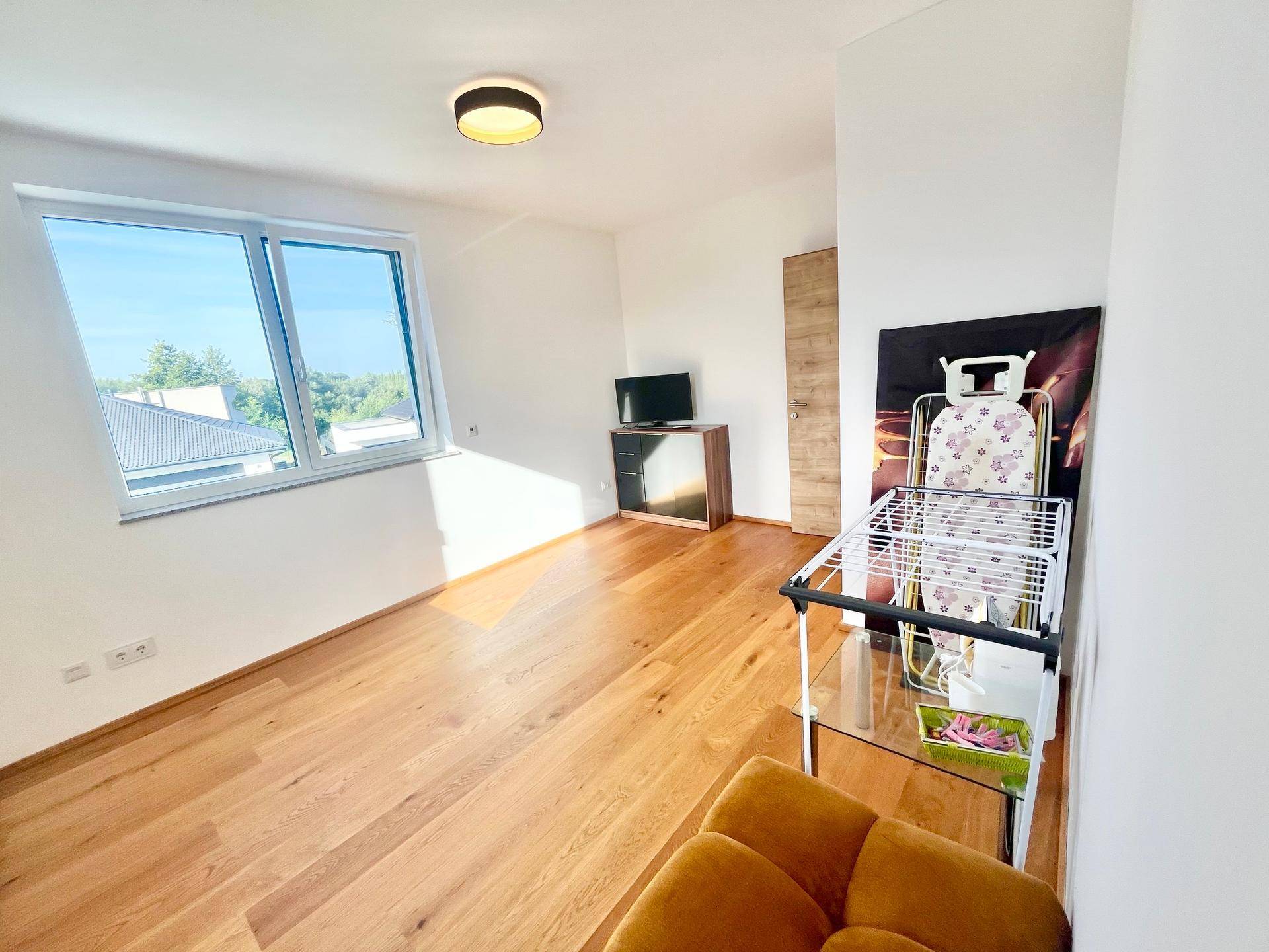 Geräumiges Schlafzimmer mit Holzboden, viel Tageslicht und Blick ins Grüne.
