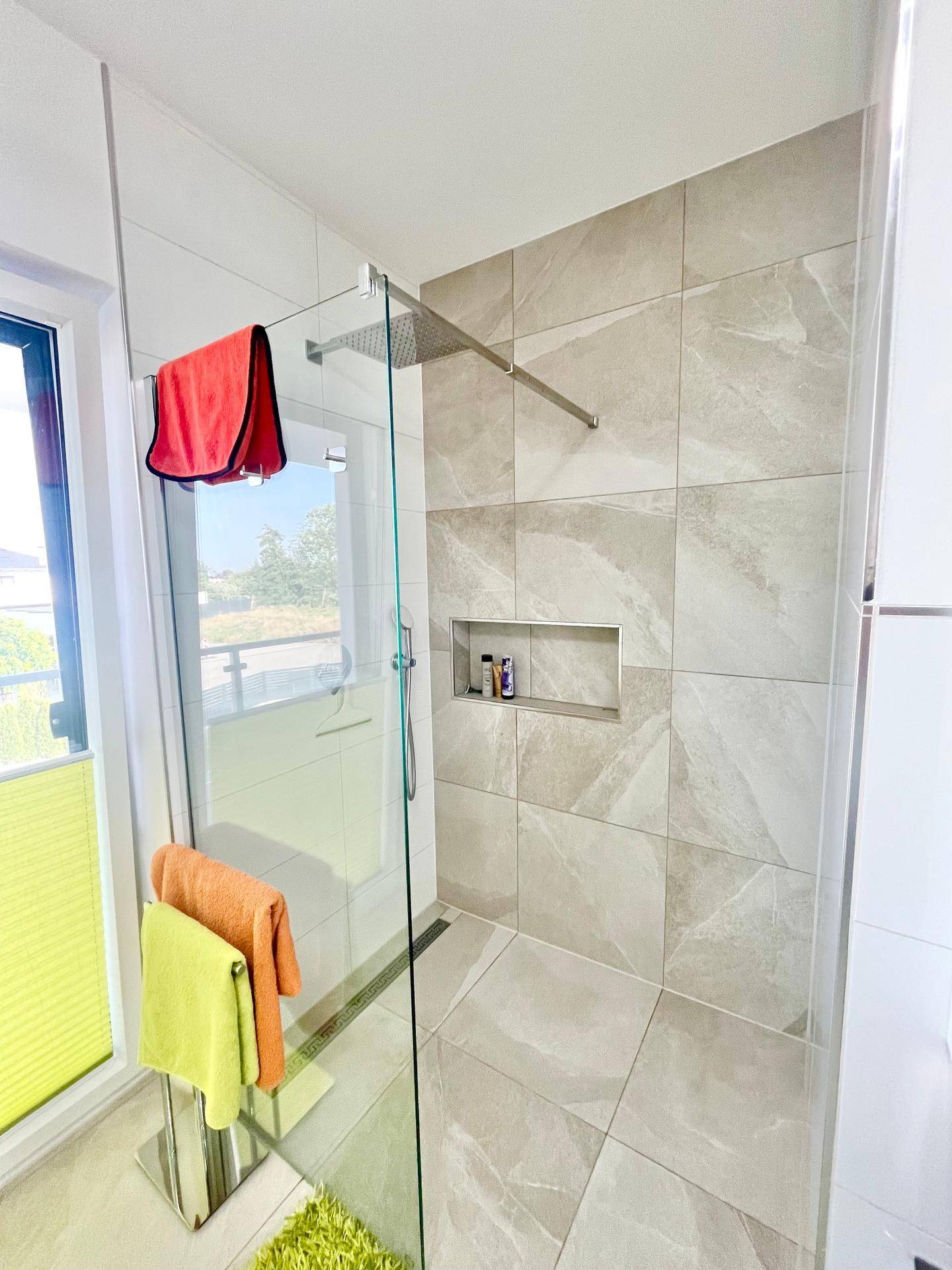 Geräumige, begehbare Dusche mit Regenduschkopf und großformatigen Fliesen in hellem Design.