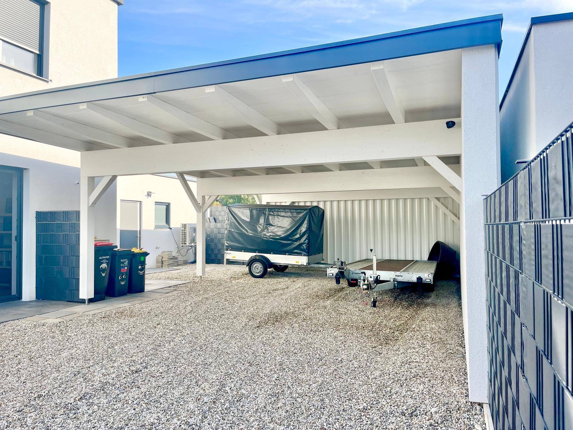 Geräumiger Carport mit Kiesboden, bietet Platz für Fahrzeuge und einen Lagercontainer.