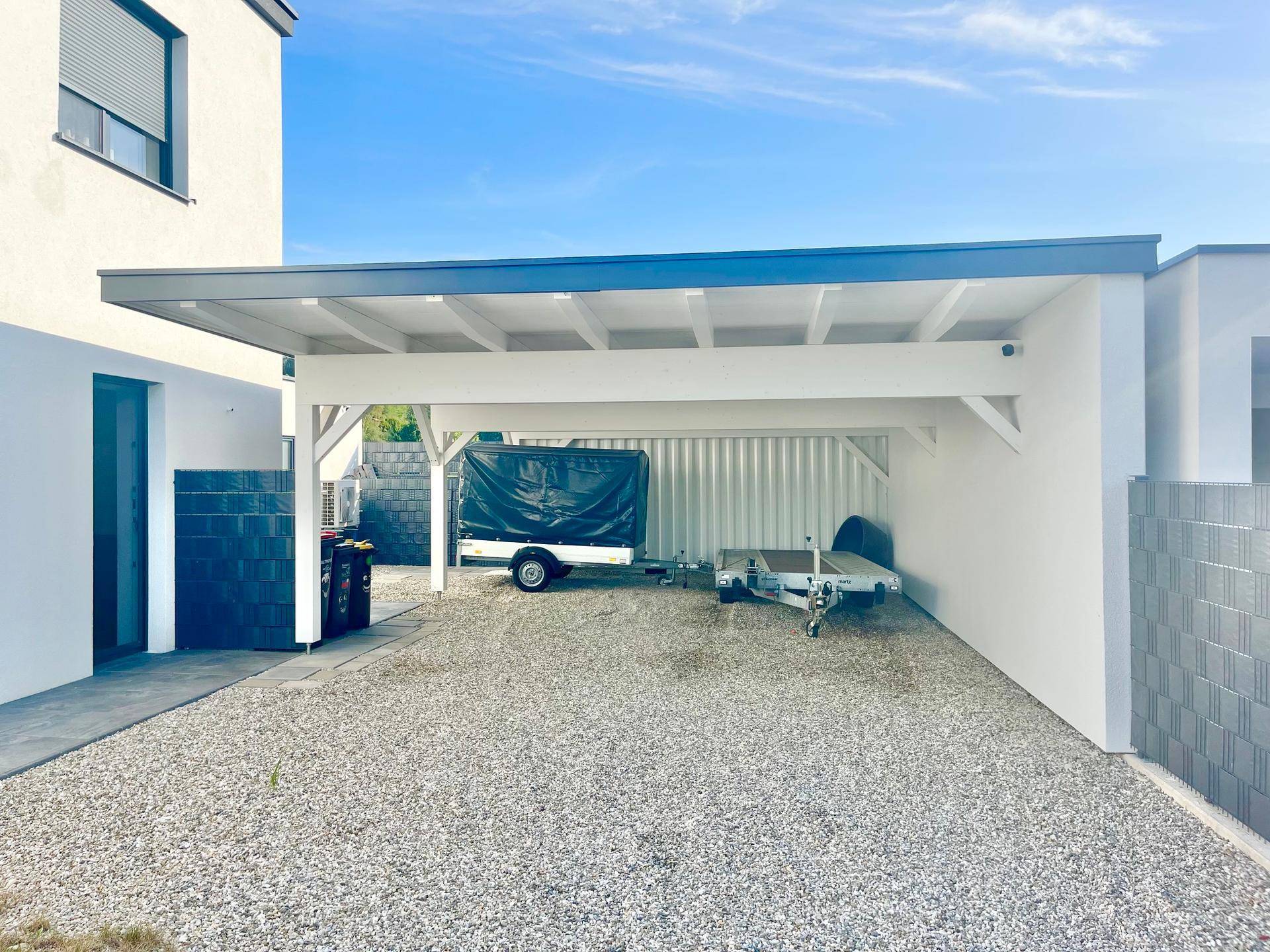 Weitläufiger Carportbereich mit stabiler Überdachung und Kiesfläche für mehrere Fahrzeuge.
