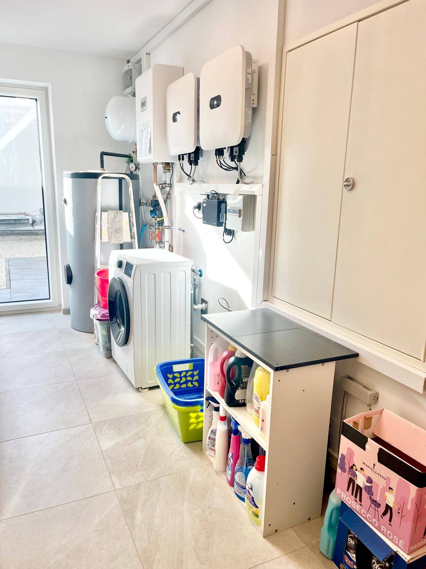 Hauswirtschaftsraum mit Waschmaschine, Warmwasserboiler und Photovoltaik-Wechselrichtern.