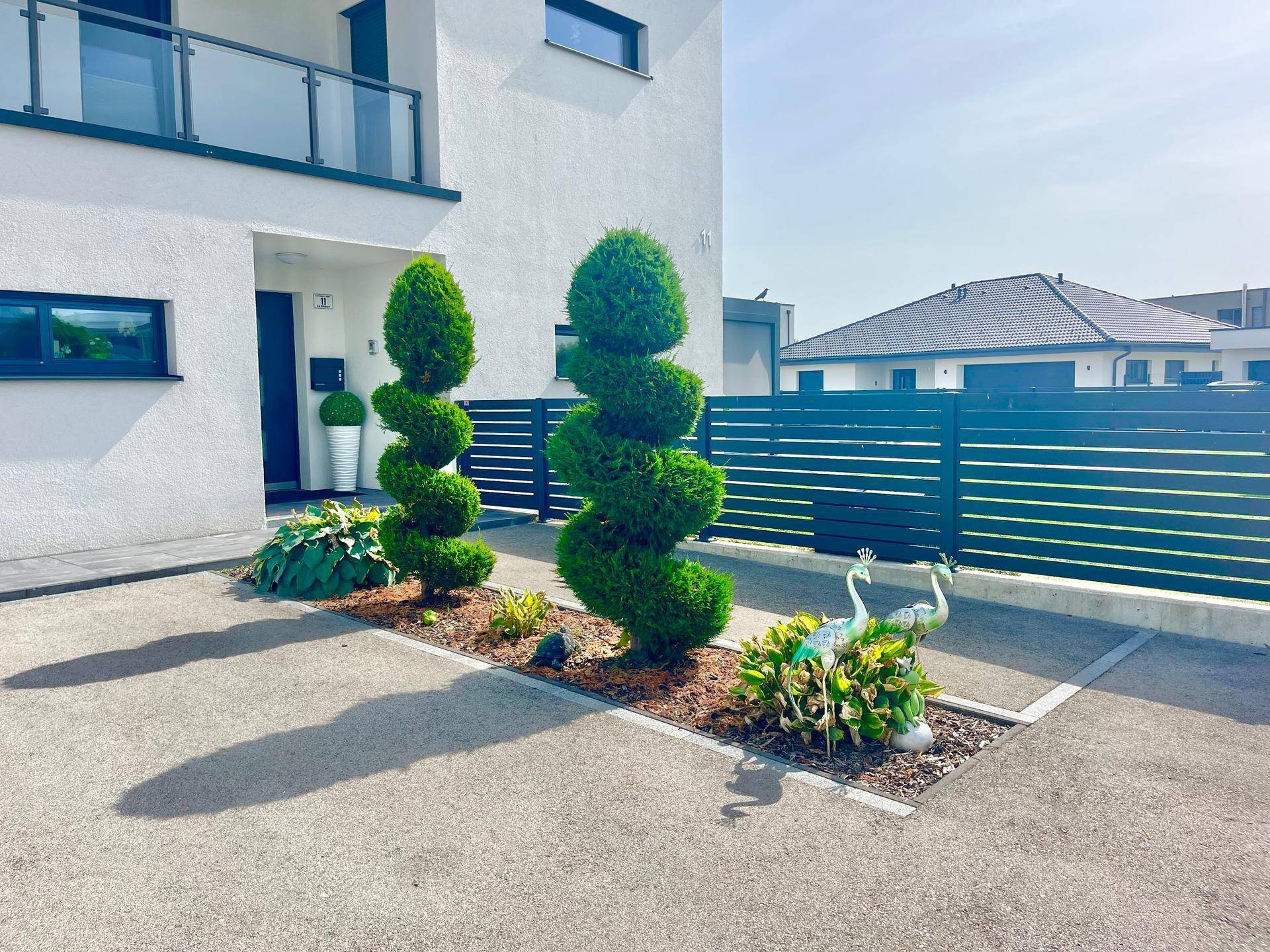 Nahaufnahme der dekorativen Formschnittpflanzen und Gartenornamente im Eingangsbereich des Hauses.