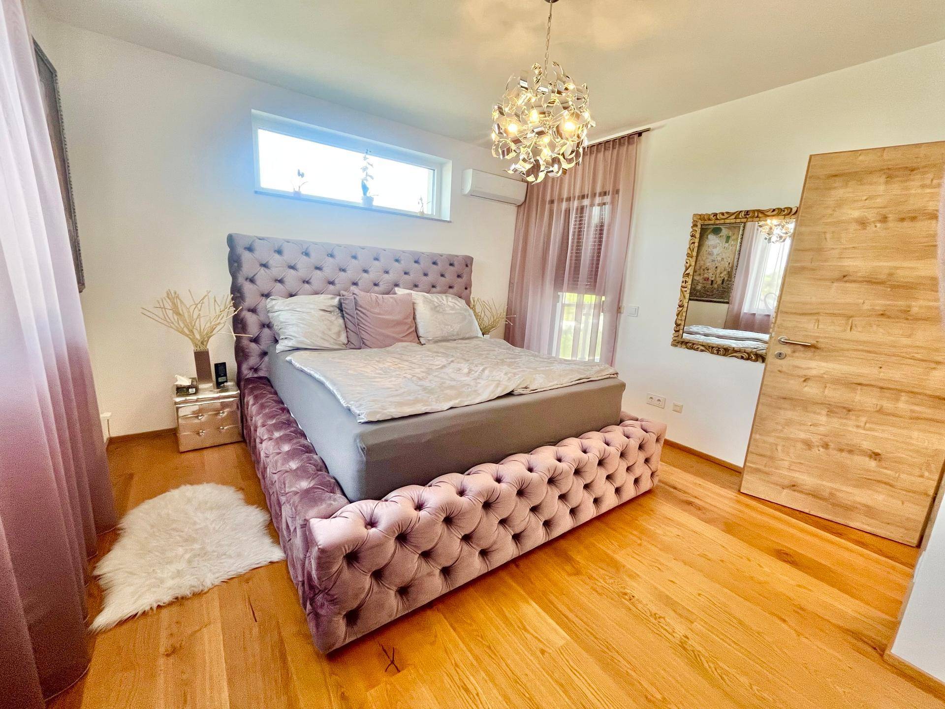 Schlafzimmer mit gepolstertem Bett, Holzboden und großem Spiegel.
