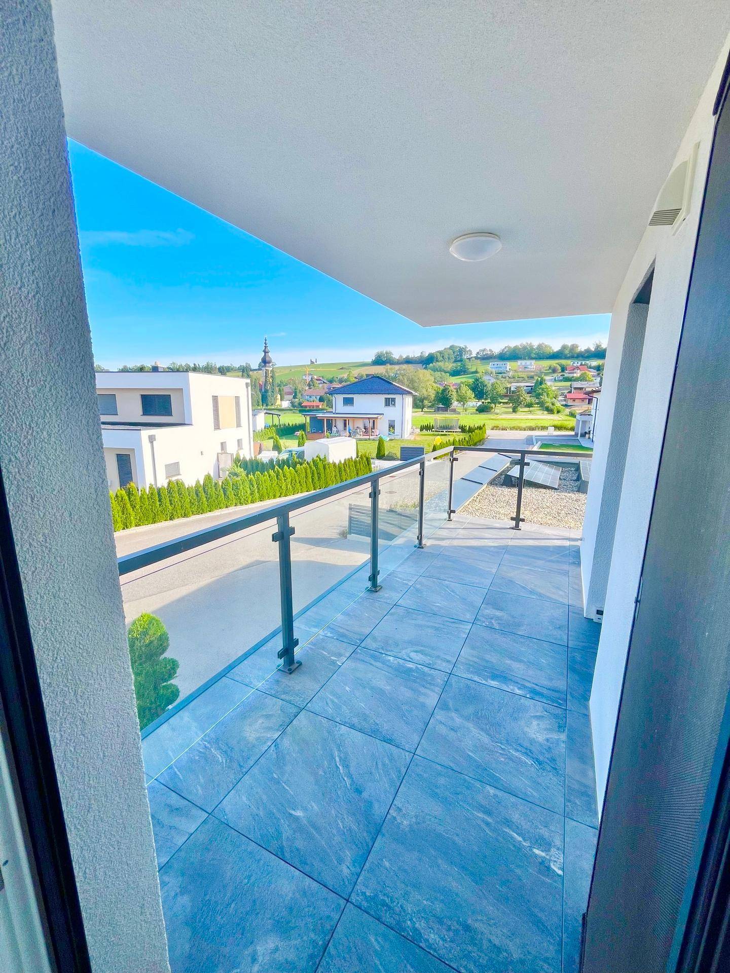 Geräumiger Balkon mit Fliesenboden und Glasgeländer, bietet einen weiten Blick über die Landschaft.